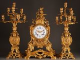 a gold clock and three candelabs on a black background