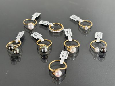 six pairs of pearl and gold rings on a black surface