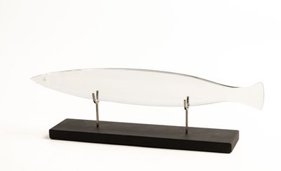 un poisson en verre posé sur un socle en bois, sur fond blanc