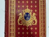 un vieux livre rouge aux tranches dorées, orné d'un blason bleu sur la couverture