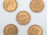 five gold coins of different sizes and shapes on a white surface