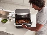 a man standing in front of an air fryer with food in it
