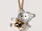 un petit ours en peluche avec une chaîne en or, posé sur une surface blanche