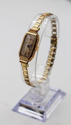 un gros plan d'une montre-bracelet en or posée sur un socle transparent