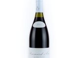 the bottle of red wine is sitting on a white surface