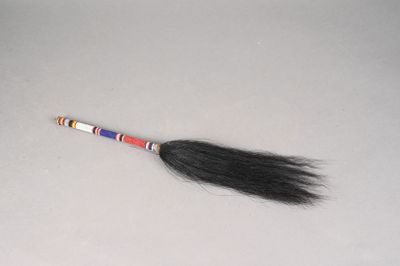 un long cheveu noir fixé sur un bâton, posé sur une surface blanche