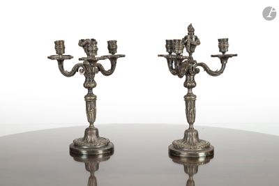une paire de bougeoirs anciens en métal argenté posés sur une table en verre