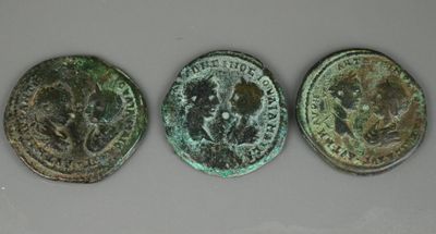 trois pièces de monnaie romaines anciennes, dont l'une représente une tête de lion et l'autre est une