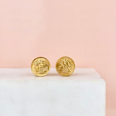 a pair of gold coin stud earrings sitting on top of a marble block