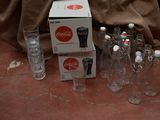 Des bouteilles et des verres sont posés par terre à côté d'une caisse de Coca-Cola.