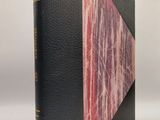 un vieux livre avec une couverture rose et noire posée sur une surface blanche