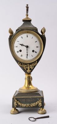 une horloge dorée et noire posée sur un socle, avec une paire de ciseaux
