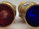 pair of vases sitting on a white surface with a red and blue glass