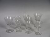six clear wine glasses are lined up on a white surface