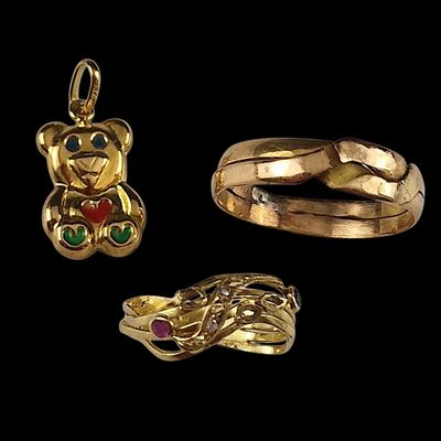 deux bagues en or et un pendentif en forme d'ours en peluche sur fond noir