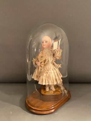 une image représentant une poupée placée sous un dôme en verre posé sur un socle en bois