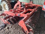 une charrue rouge posée dans la terre à côté d'un tracteur