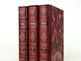 trois livres rouges sont empilés sur une surface blanche