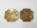 two brass plaques of birds and flowers on a white surface