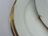 two white plates with gold rims sit on a white surface