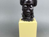 une sculpture noire représentant une tête de bélier posée sur un socle jaune