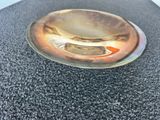 une assiette en argent sur laquelle est représenté un poisson, posée sur un fond noir
