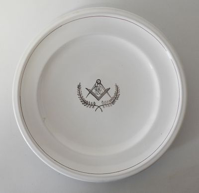 une assiette blanche ornée d'un emblème maçonnique