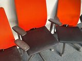 three orange and black office chairs are lined up against a white wall