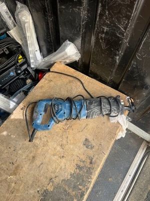 une perceuse bleue posée par terre à côté d'autres outils