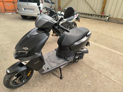 un scooter garé sur un parking, avec une voiture en arrière-plan
