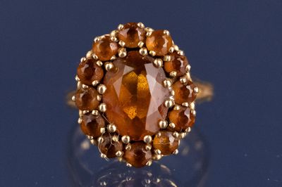 une image représentant une bague ornée d'une grosse pierre orange entourée de petites boules en or