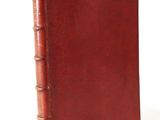 an old book with a red cover sitting on top of a white surface