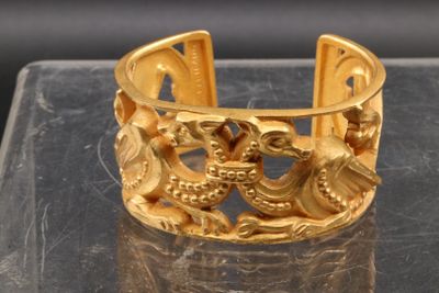 un bracelet en or orné de deux oiseaux, posé sur une table