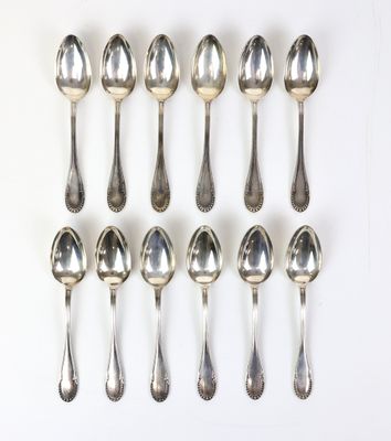 six cuillères en argent sont disposées en ligne sur une surface blanche