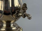 a silver coffee pot sitting on top of a table next to a lamp