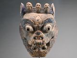 un masque orné d'un crâne, posé sur un socle