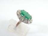 an oval emerald and diamond ring on a clear display stand