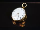 une montre de poche en or posée sur une pile de pièces de monnaie