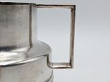 a silver pitcher with a handle on a white surface
