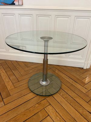 une table en verre avec un piètement en métal posée sur un parquet