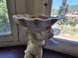 une statue représentant un chat assis dans un bol, posé sur le rebord d'une fenêtre