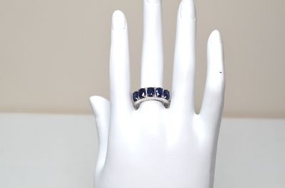 a white hand holding a ring with blue stones on it