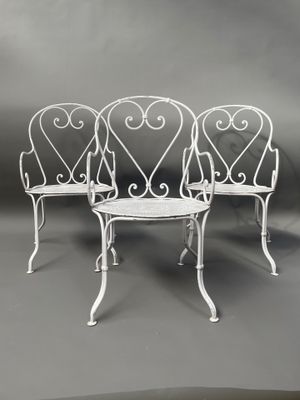 trois chaises blanches en fer forgé et une table sur fond gris