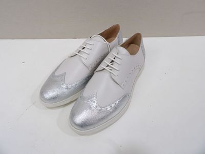 white leather shoes with silver laces on top of a white surface