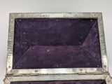 an old silver metal box with purple velvet lining on a white surface