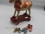un petit cheval en peluche sur un skateboard, à côté d'une paire de chaussures de bébé