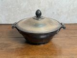 une cocotte ancienne en métal argenté avec son couvercle, posée sur une table en bois