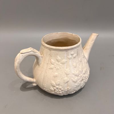 une petite théière blanche avec une anse, posée sur une table