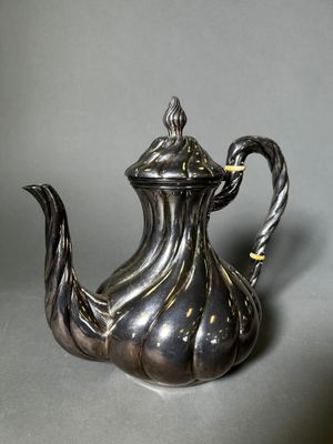 une théière ancienne en argent, dotée d'une anse torsadée sur un fond gris