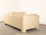 a beige leather couch sitting in a corner of a room